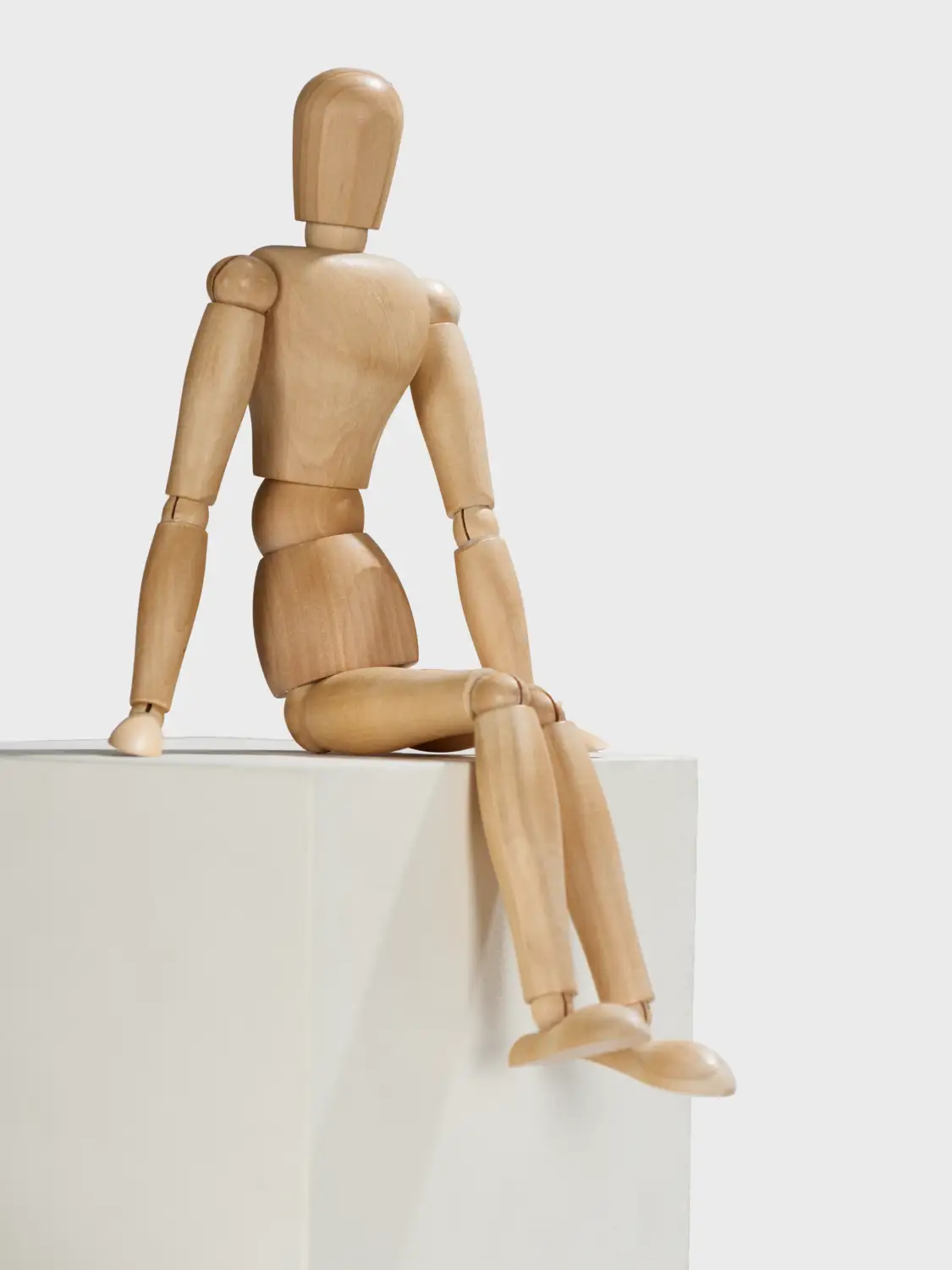 Gliederpuppe aus Holz, die auf einem weißen Sockel sitzt