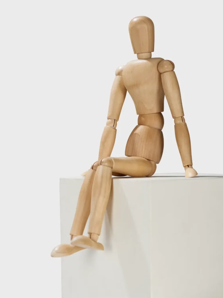 Gliederpuppe aus Holz, die auf einem weißen Sockel sitzt
