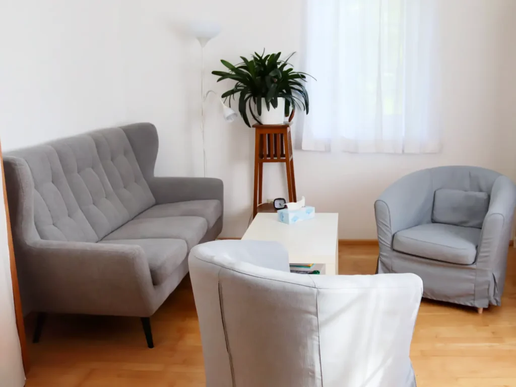 Helles Zimmer mit grauem Sofa, zwei Sesseln, weißem Couchtisch und einer Zimmerpflanze